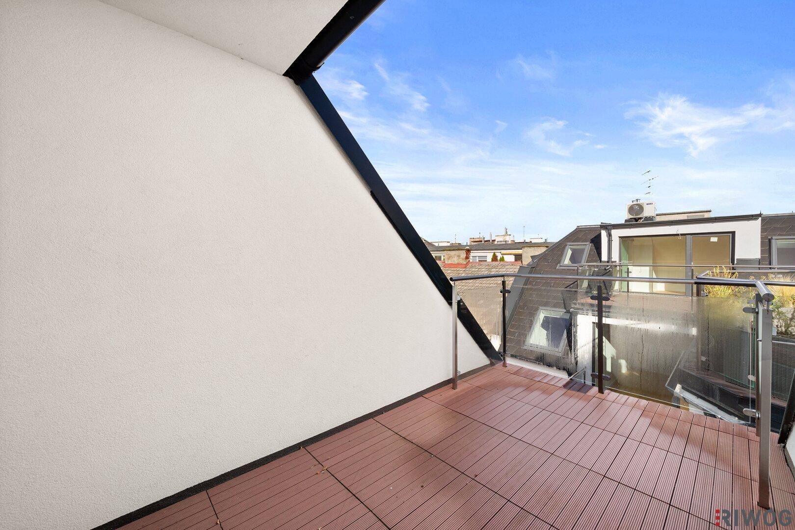 Moderner Balkon mit Holzdielenboden und Glasgeländer, bietet einen weiten Blick über die Dächer der Stadt.
