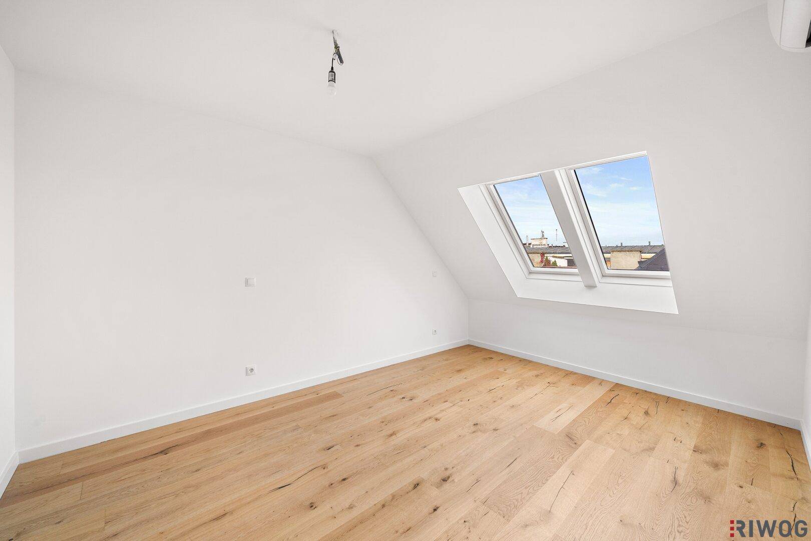 Lichtdurchflutetes Zimmer im Dachgeschoss mit Holzboden und großen Dachfenstern, bietet viel Tageslicht.