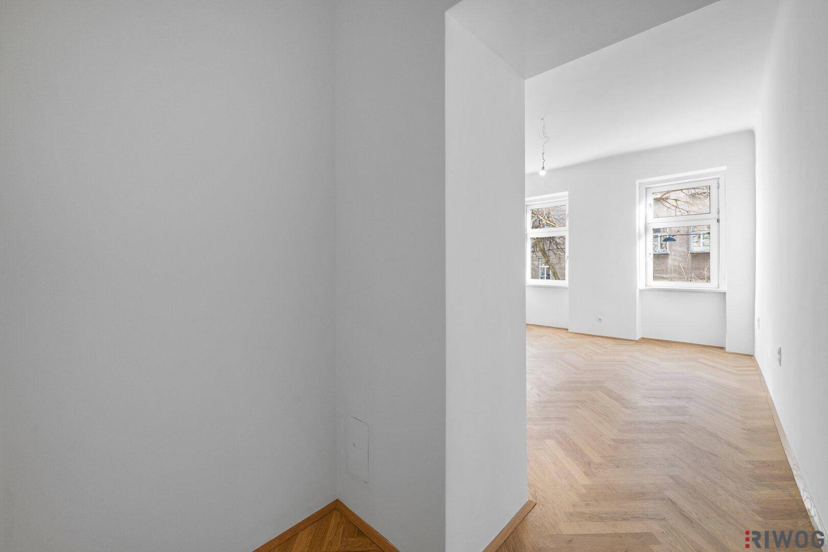 Heller Flur mit Fischgrätparkett, der zu einem weiteren Zimmer mit Fenstern führt.