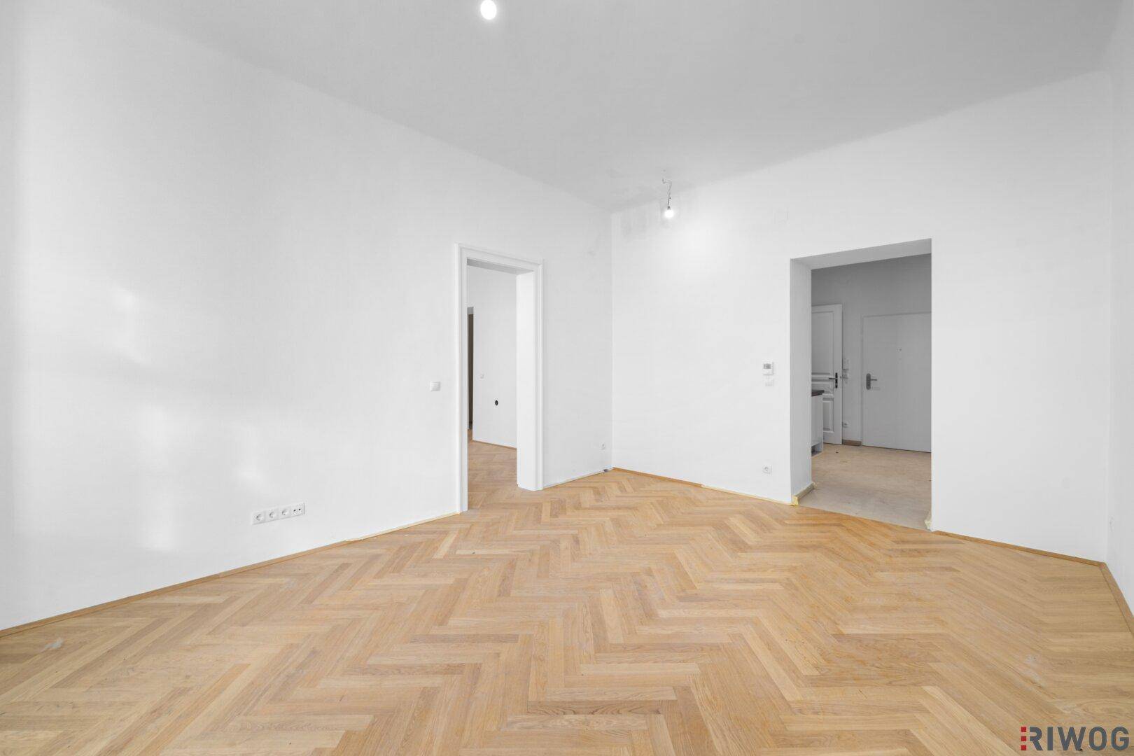 Geräumiges Zimmer mit Fischgrätparkett und mehreren Türöffnungen, ideal für flexible Nutzung.