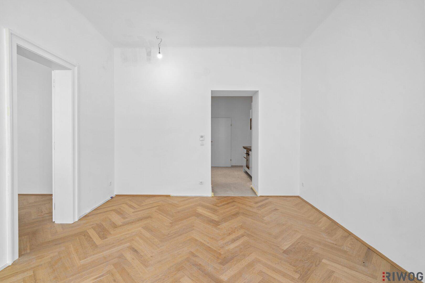 Leeres Zimmer mit Fischgrätparkett und Zugang zu weiteren Räumen, bereit zur Einrichtung.