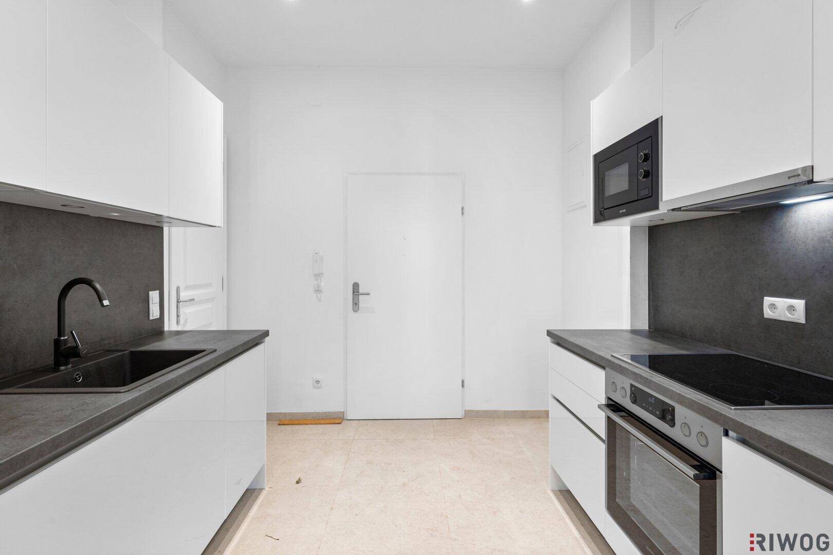 Moderne Küche mit weißen Hochglanzschränken, dunkler Arbeitsplatte und integrierten Geräten.