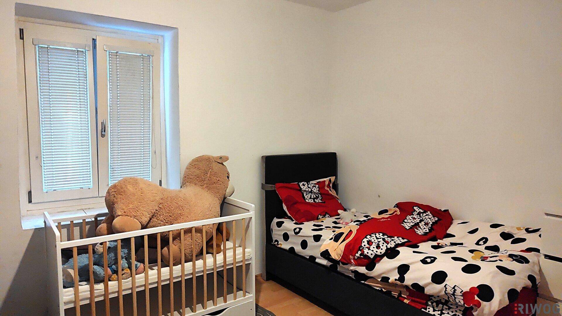 Kinderzimmer mit Kinderbett, Einzelbett und hellem Fenster, dekoriert mit Spielzeug.
