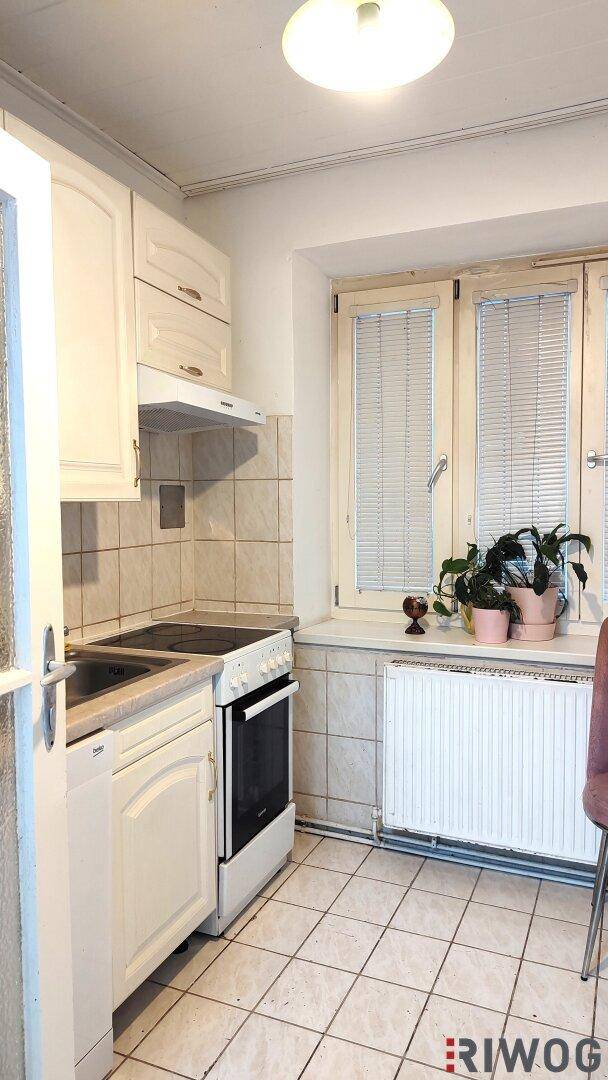 Helle Küche mit weißen Einbauschränken, Elektroherd und gefliestem Boden sowie einem Fenster.