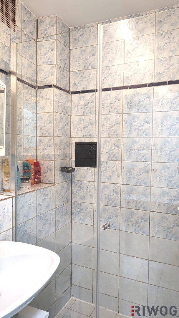 Badezimmer mit Duschkabine, weißem Waschbecken und hellblauen Fliesen an Wänden und Boden.