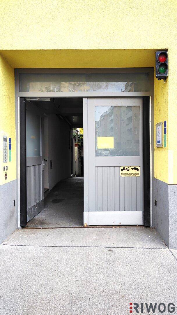 Eingangsbereich zu einem Gebäude mit gelber Fassade und geöffneter Tür, daneben eine Ampel.