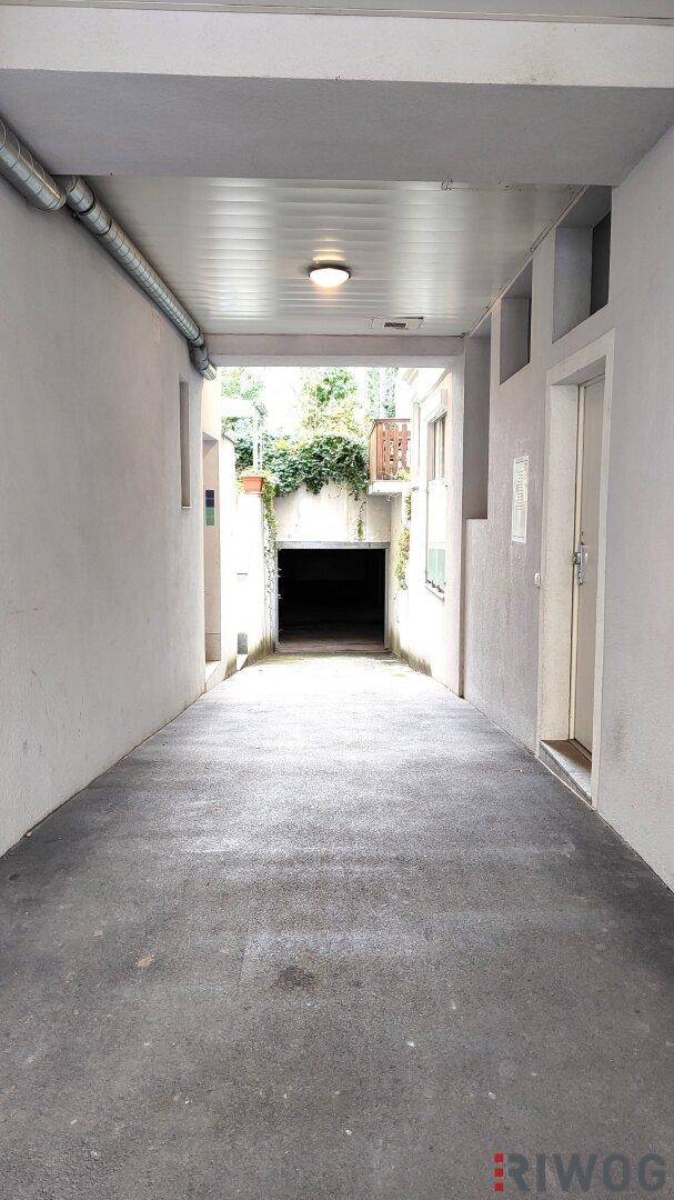 Langer, schmaler Durchgang führt zu einem Garagentor, mit einem kleinen Balkon am Ende des Hofes.
