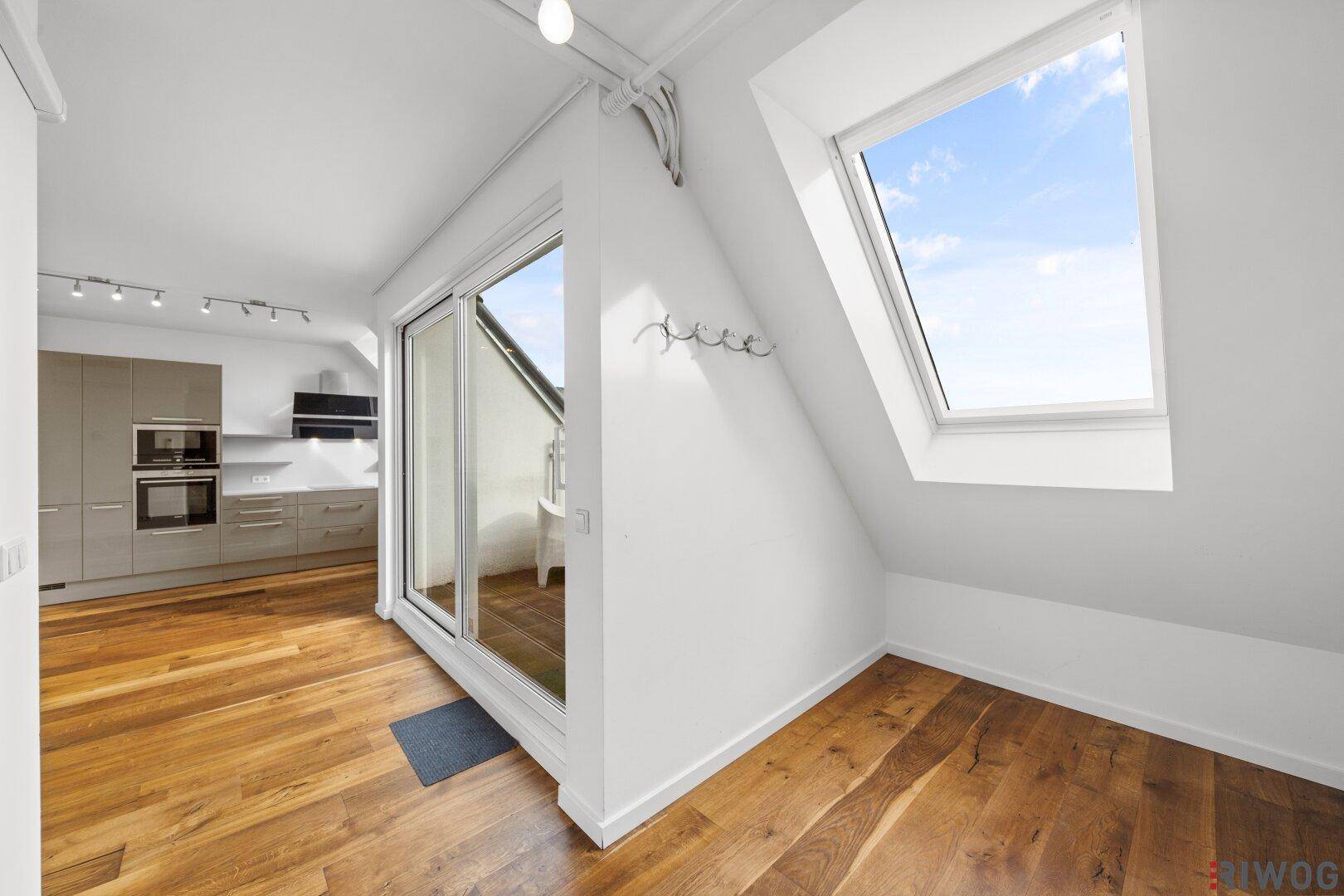 Heller Wohnbereich mit Holzboden, Dachfenster und Zugang zum Balkon.