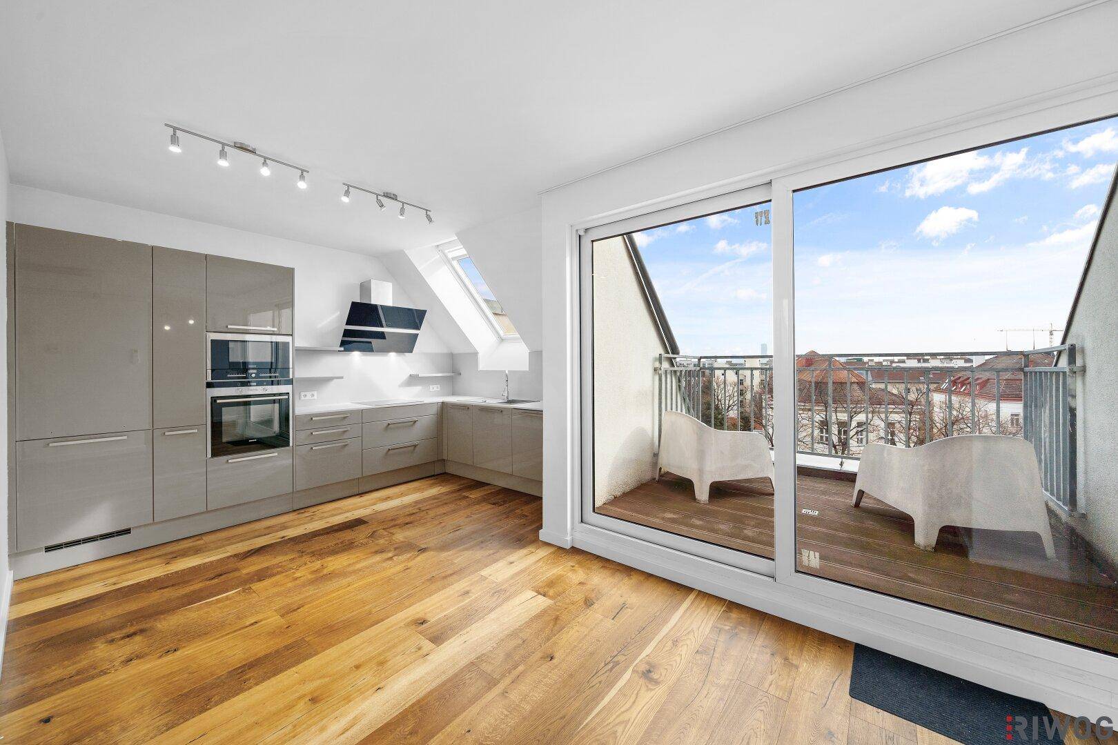 Moderne offene Küche mit glänzenden Schränken, Holzboden und Zugang zu einem kleinen Balkon.