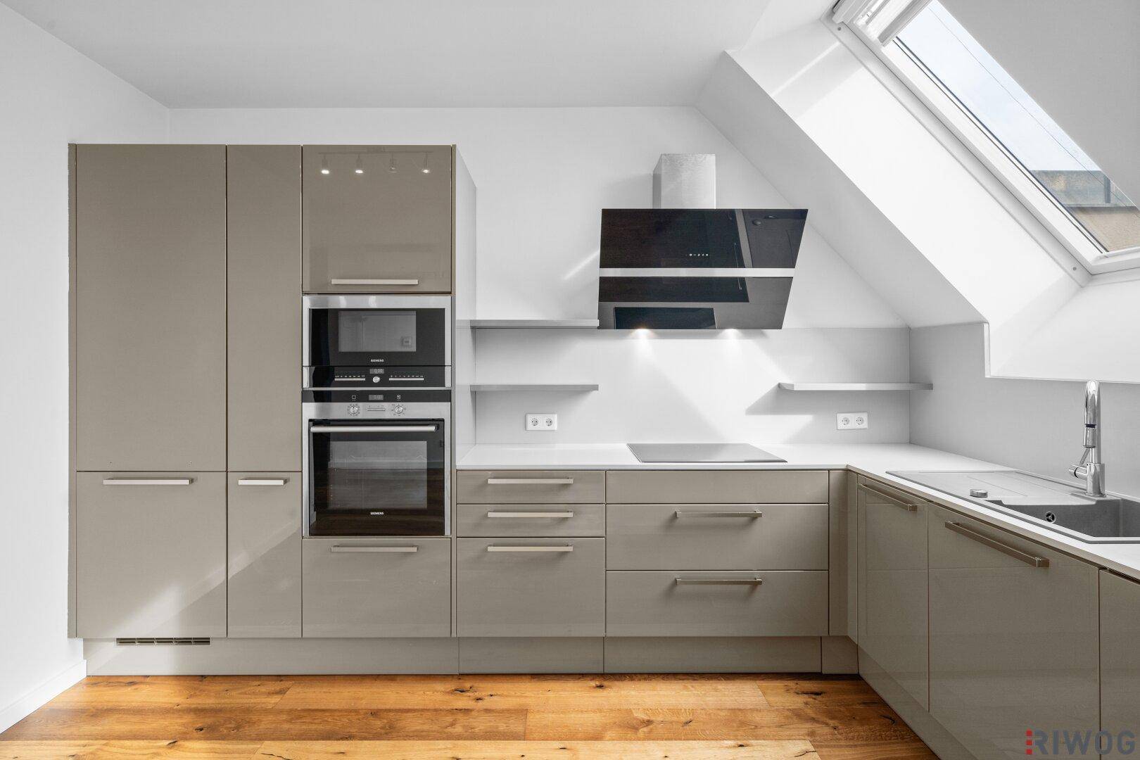 Moderne Einbauküche mit grauen Hochglanzfronten, integrierten Geräten und Dachfenster.