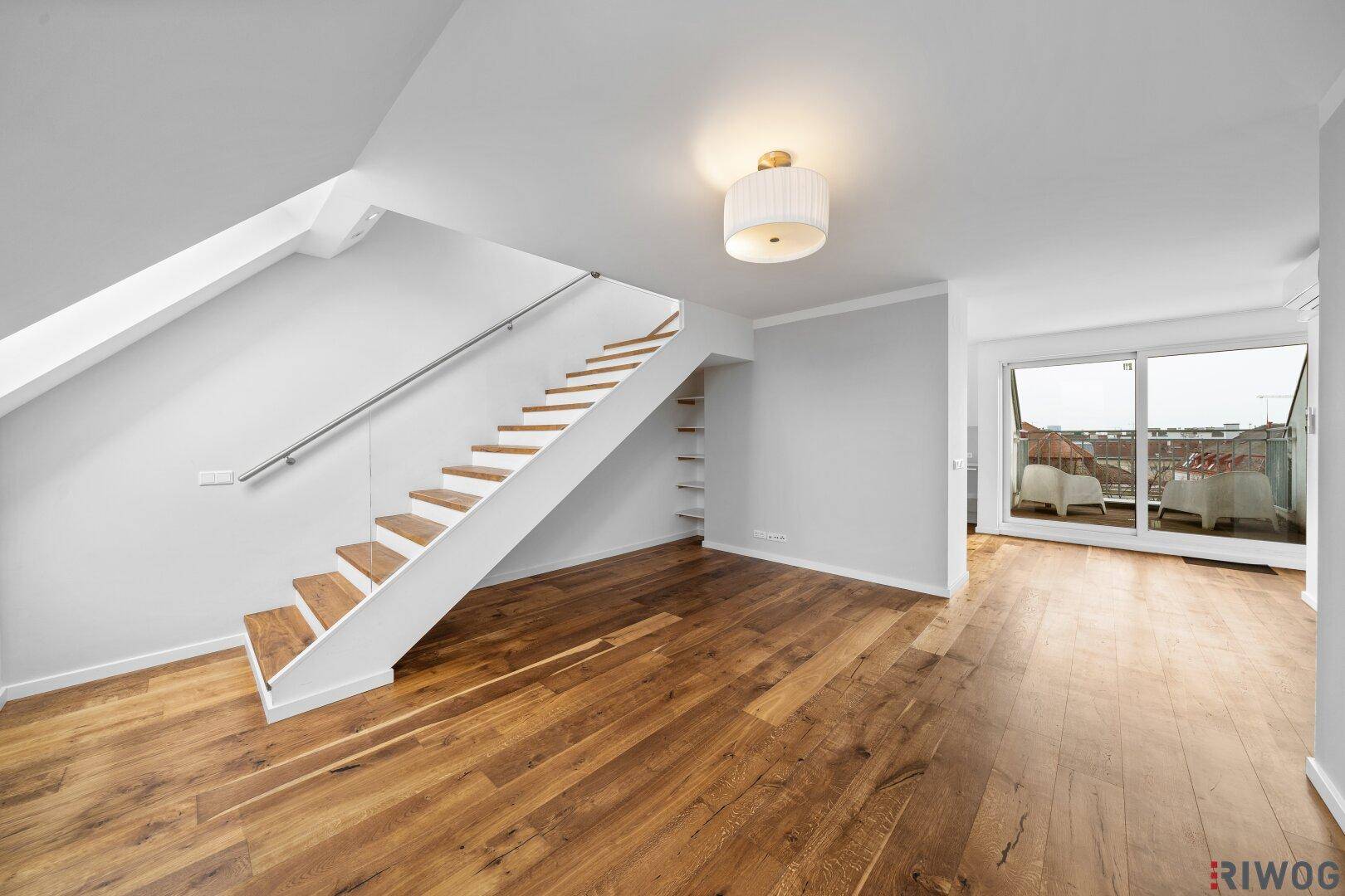 Geräumiger Wohnbereich mit Holztreppe, Holzboden und Zugang zu einem Außenbereich.