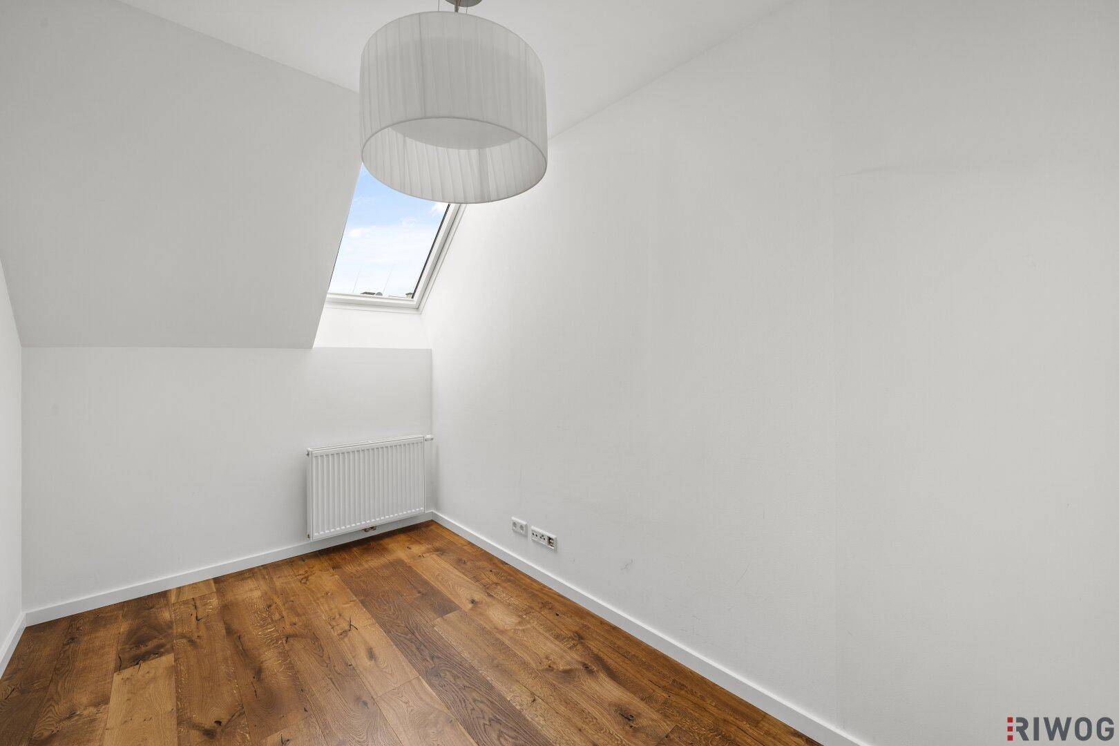 Kleines Zimmer mit Holzboden, Dachfenster und weiß gestrichenen Wänden.