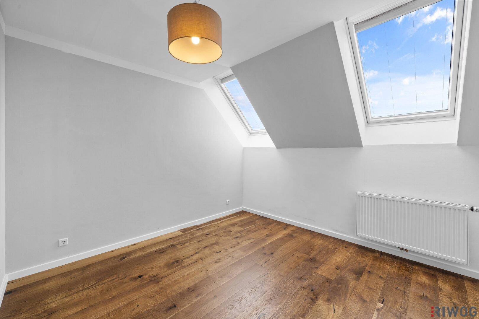 Schlafzimmer mit Holzboden, Heizkörper und zwei Dachfenstern für viel Helligkeit.