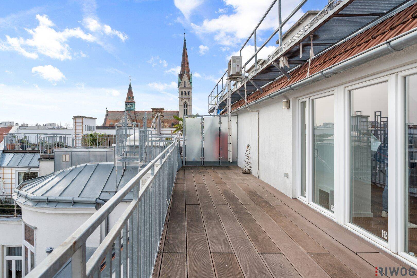 Lange Dachterrasse mit Holzboden und Blick auf die Stadt und eine Kirche.