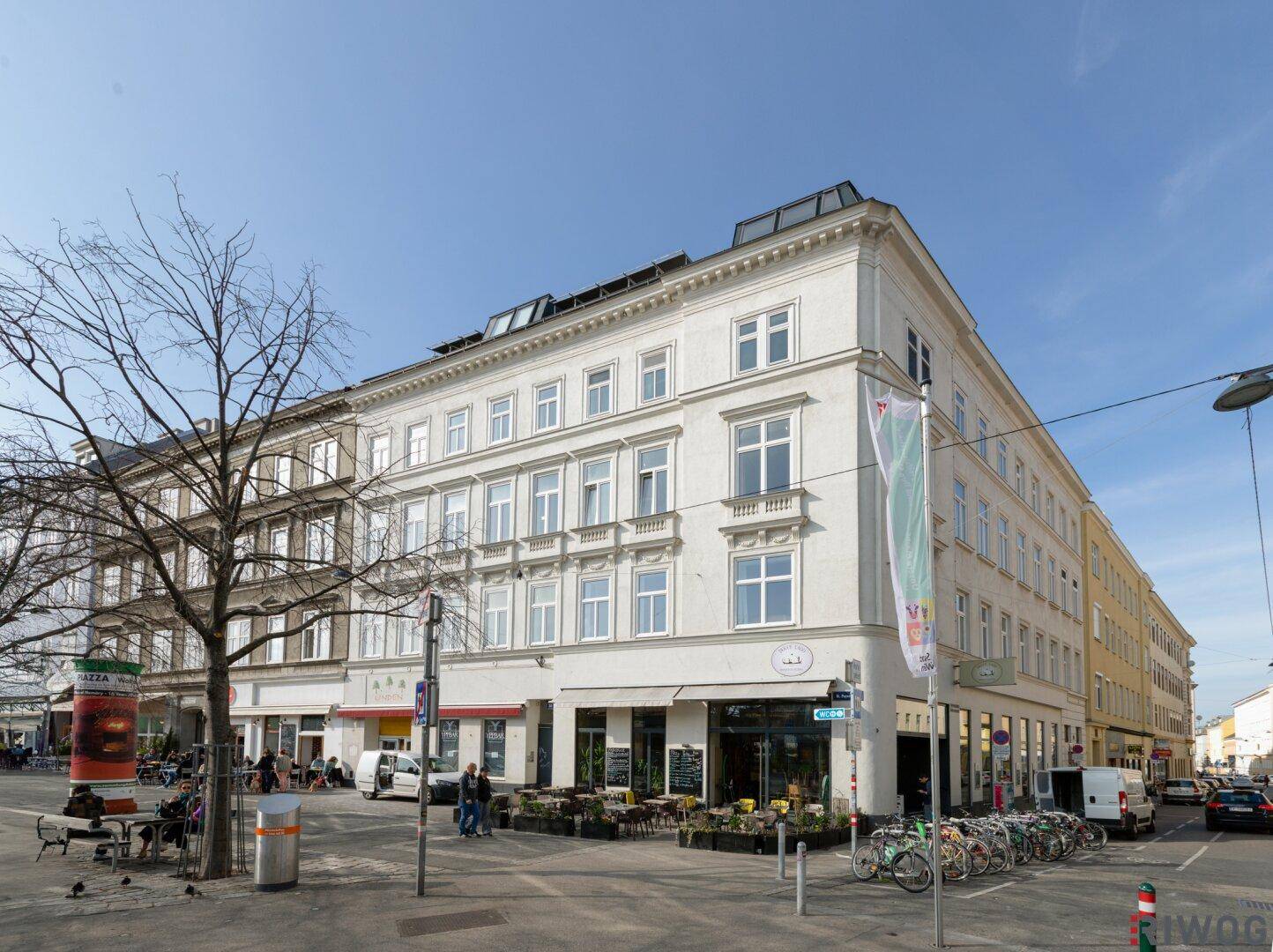 Straßenansicht eines eleganten Altbaus mit Geschäften im Erdgeschoss und großen Fenstern.