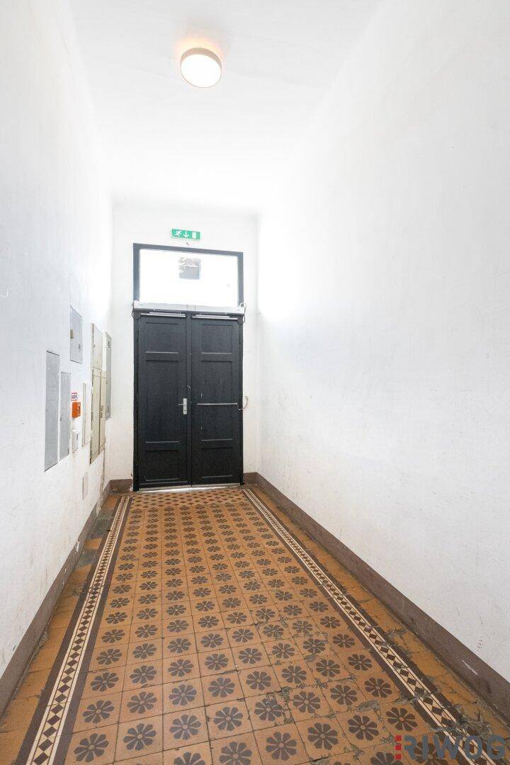 Heller Eingangsbereich mit gemusterten Fliesen und einer dunklen Eingangstür, typisch für Altbauten.