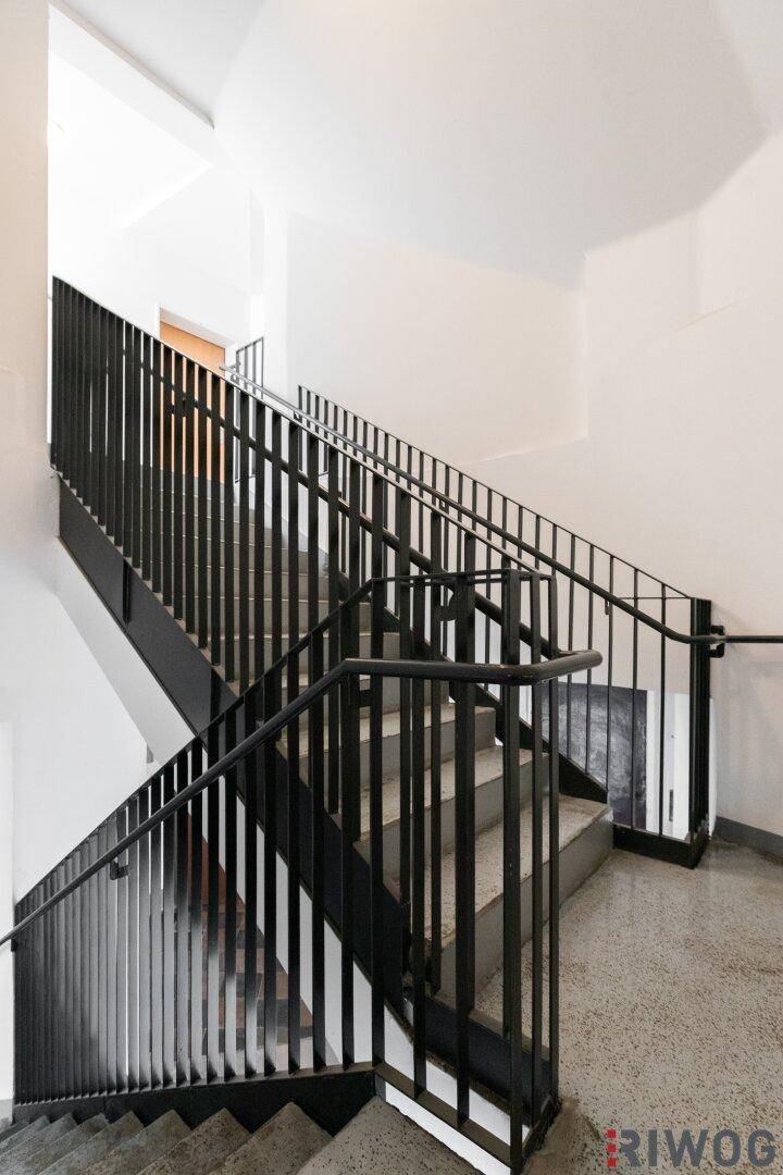 Modernes Treppenhaus mit schwarzen Metallgeländern und Steinstufen in einem hellen Gebäude.