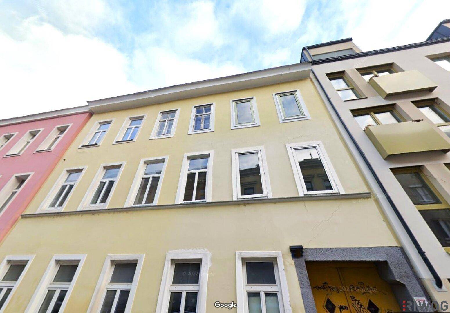 Ansicht der gelben Gebäudefassade mit vielen Fenstern und angrenzenden Häusern in der Stadt.