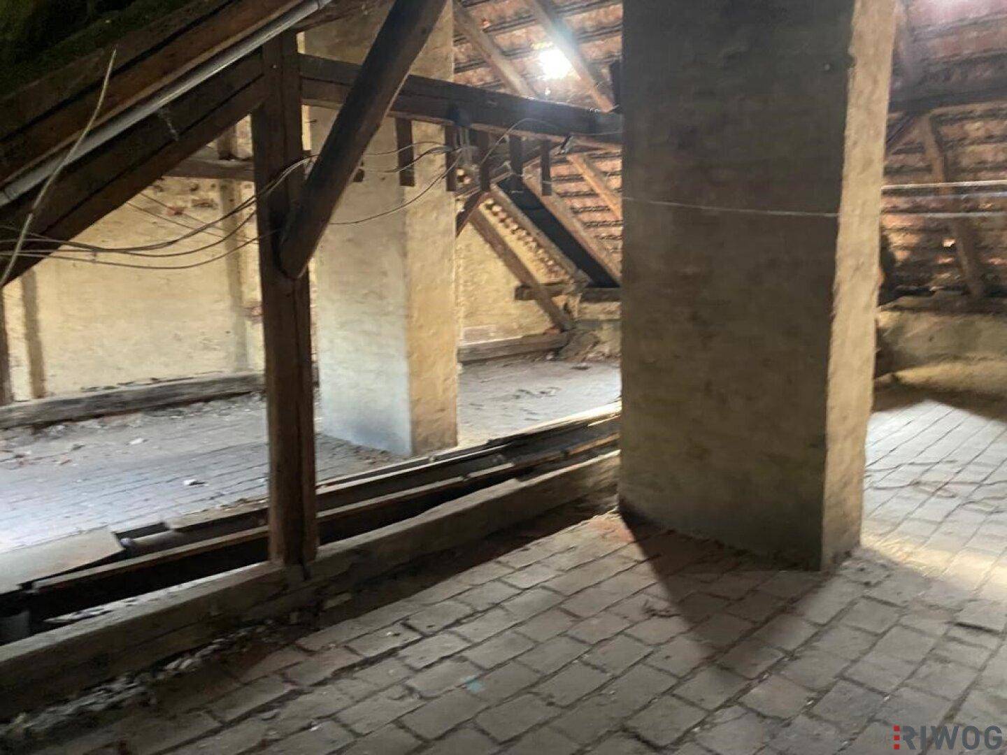 Unausgebauter Dachboden mit sichtbaren Holzbalken, Ziegelboden und Betonpfeilern, bereit für den Ausbau.