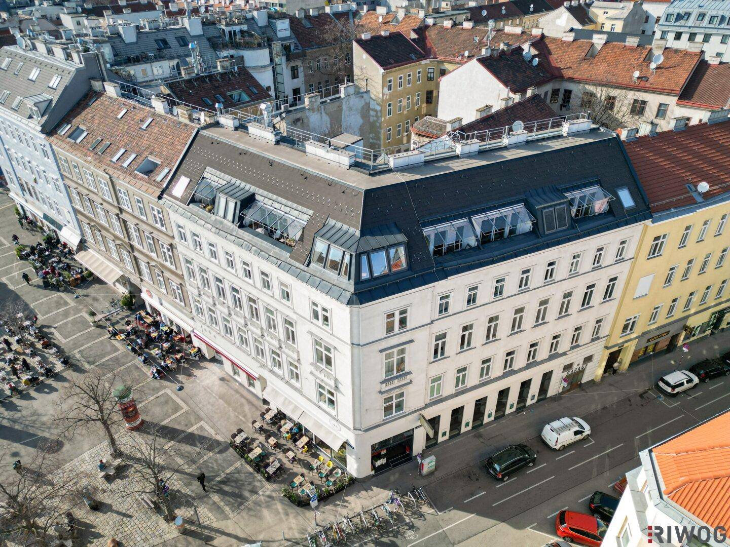Panoramablick auf ein Eckgebäude mit Mansarddach und die umliegende Stadtlandschaft unter blauem Himmel.