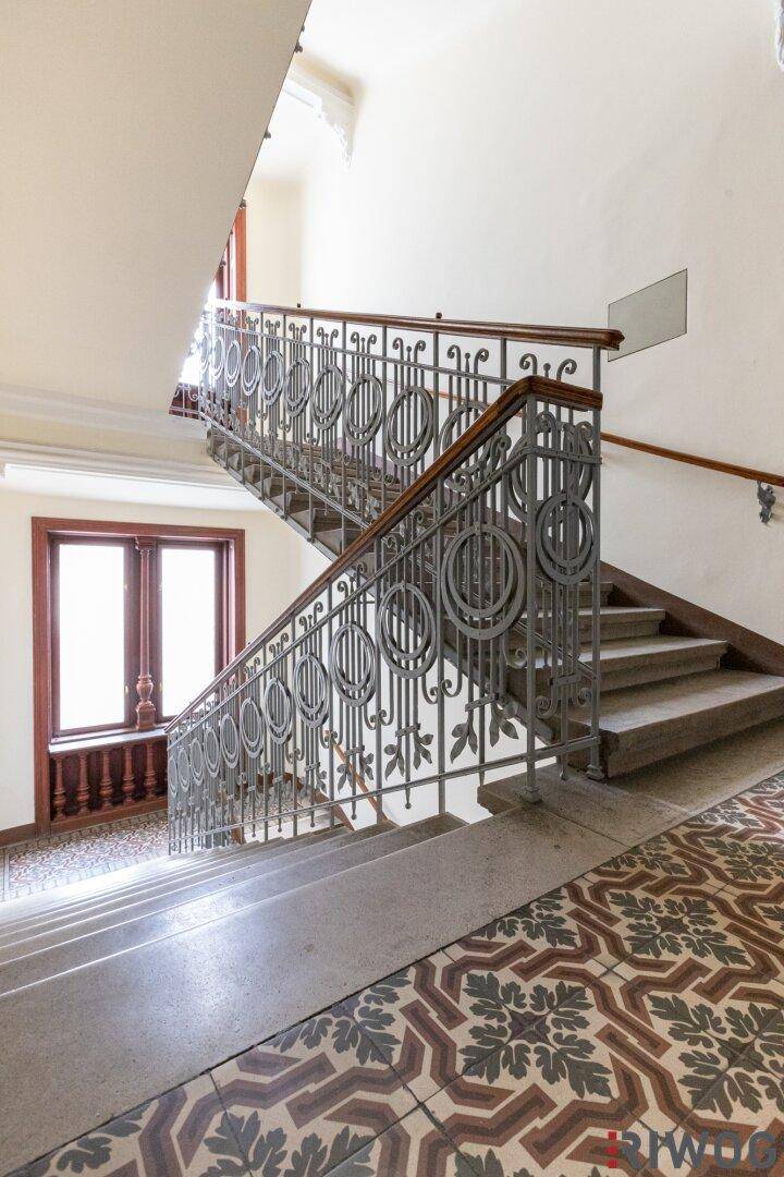 Elegantes Treppenhaus mit kunstvollem Geländer und gemusterten Fliesen, typisch für einen Altbau.