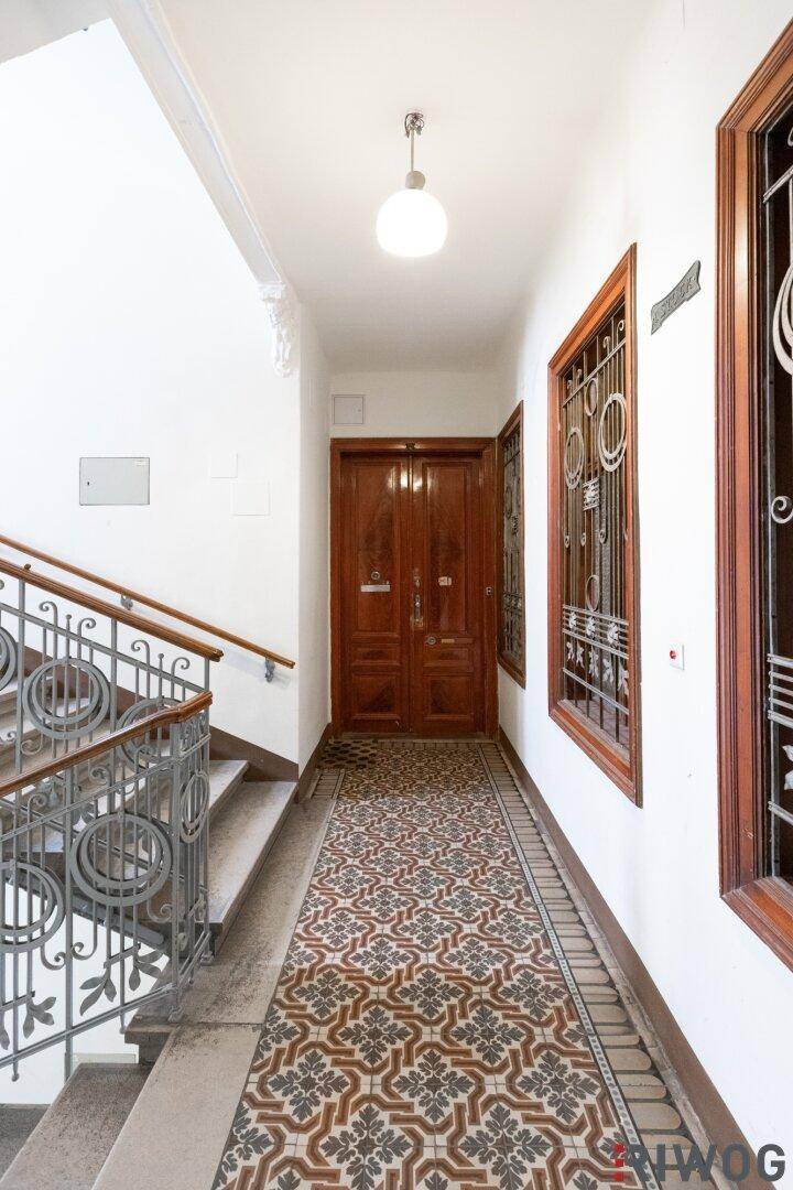Historischer Eingangsbereich mit gemusterten Fliesen und einer eleganten Treppe mit schmiedeeisernem Geländer.