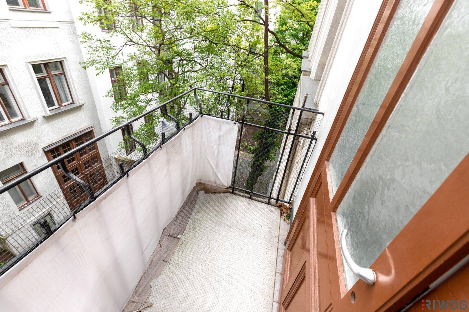 Balkon mit Fliesenboden und Blick auf den Innenhof, zugänglich durch eine Holztür.