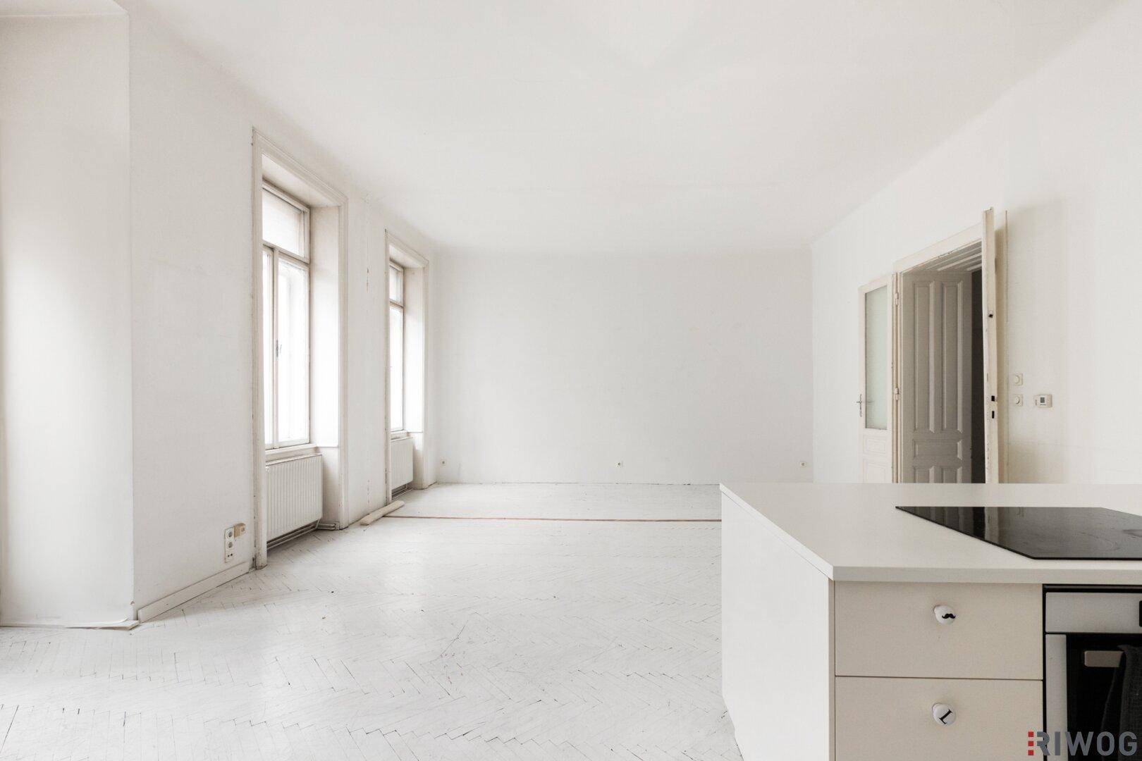 Heller Wohnbereich mit Kücheninsel und hohen Fenstern, bereit für individuelle Gestaltung.
