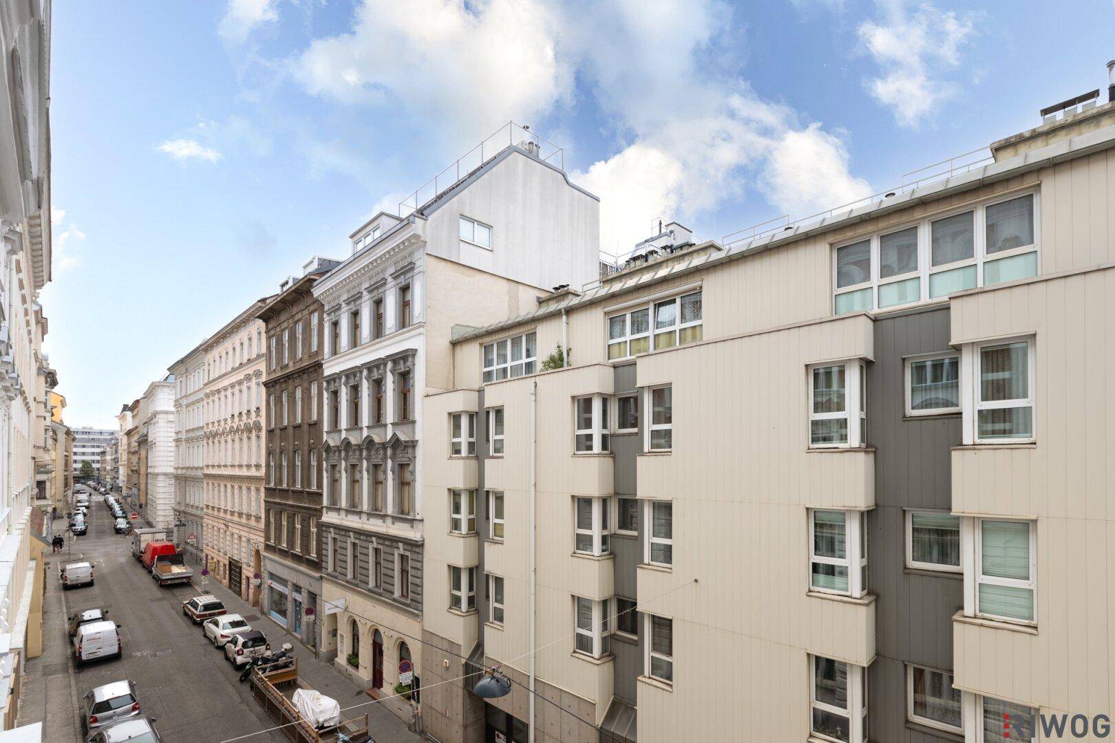 Blick auf die Straße und die Fassaden der umliegenden Gebäude mit modernen und klassischen Elementen.