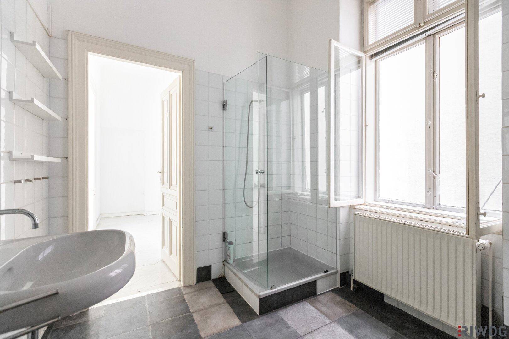 Badezimmer mit Duschkabine, Waschbecken und Fenster, das viel Tageslicht hereinlässt.