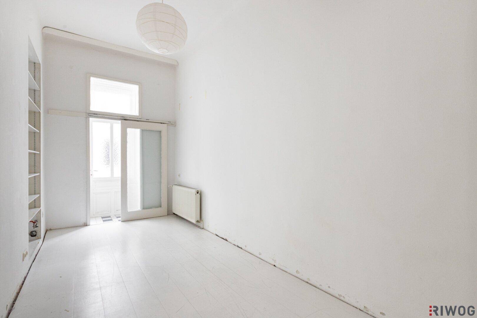 Helles Zimmer mit weiß gestrichenem Holzboden und Zugang zu einem kleinen Balkon.
