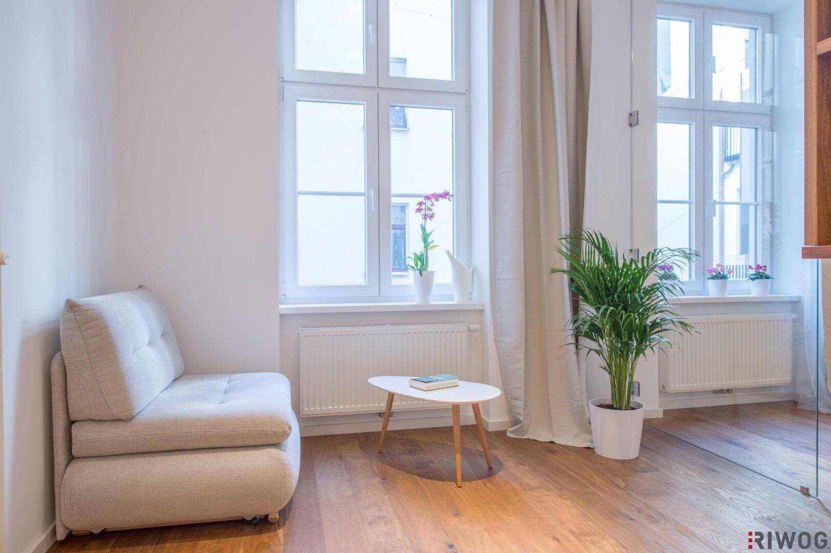 Helles Wohnzimmer mit Holzboden, großen Fenstern und einem bequemen Sessel, der zum Entspannen einlädt.