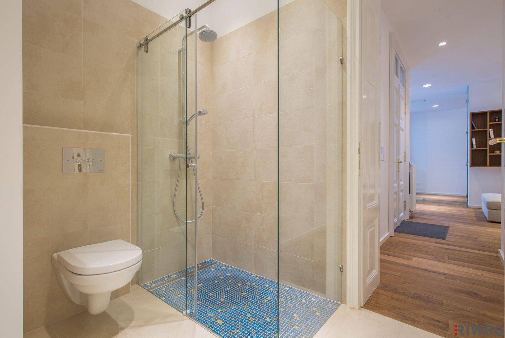 Modernes Badezimmer mit begehbarer Dusche, Wand-WC und Zugang zum offenen Wohnbereich.
