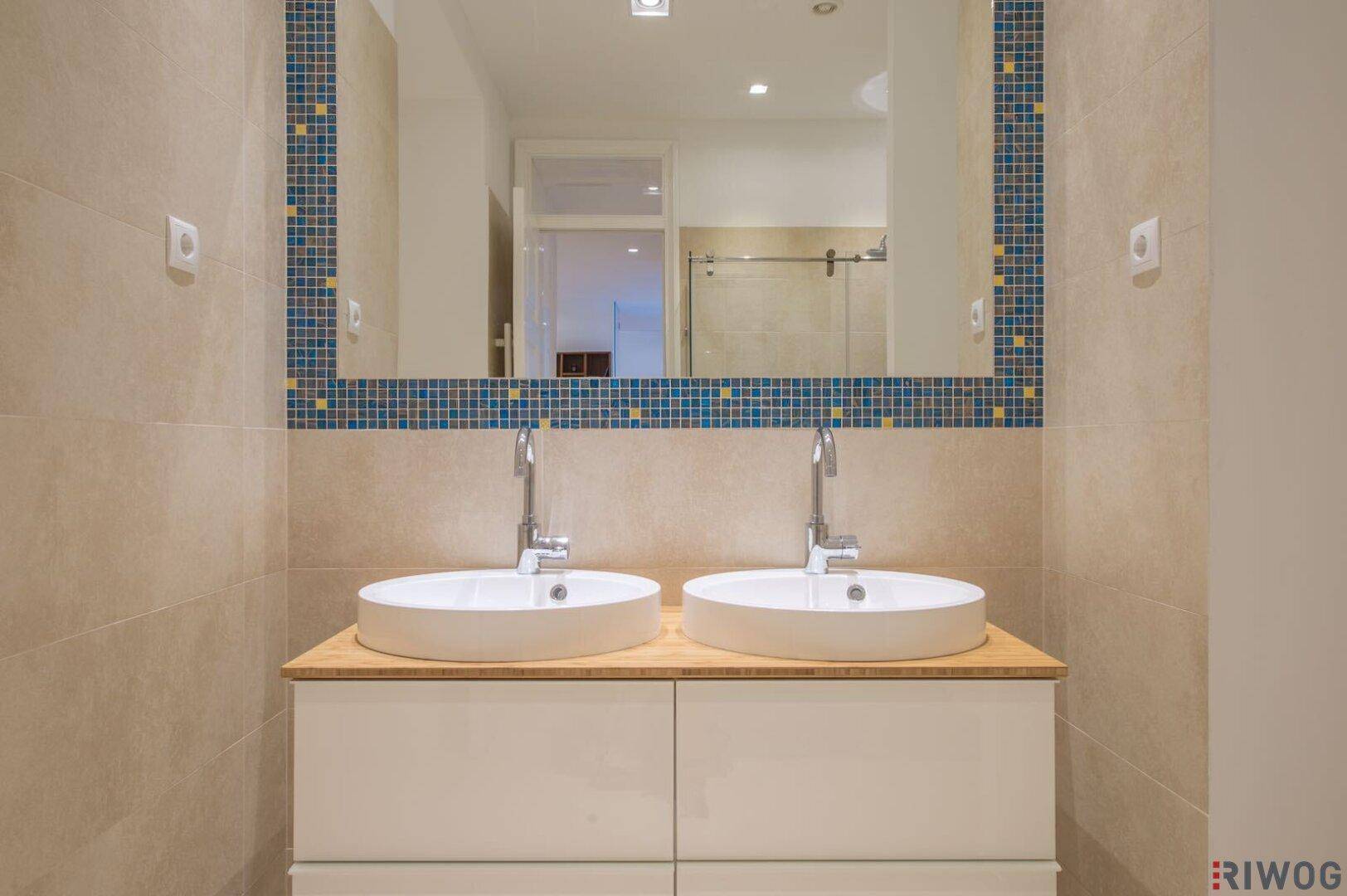 Detailansicht des modernen Badezimmers mit Doppelwaschbecken und einem Spiegel mit Mosaikrahmen.