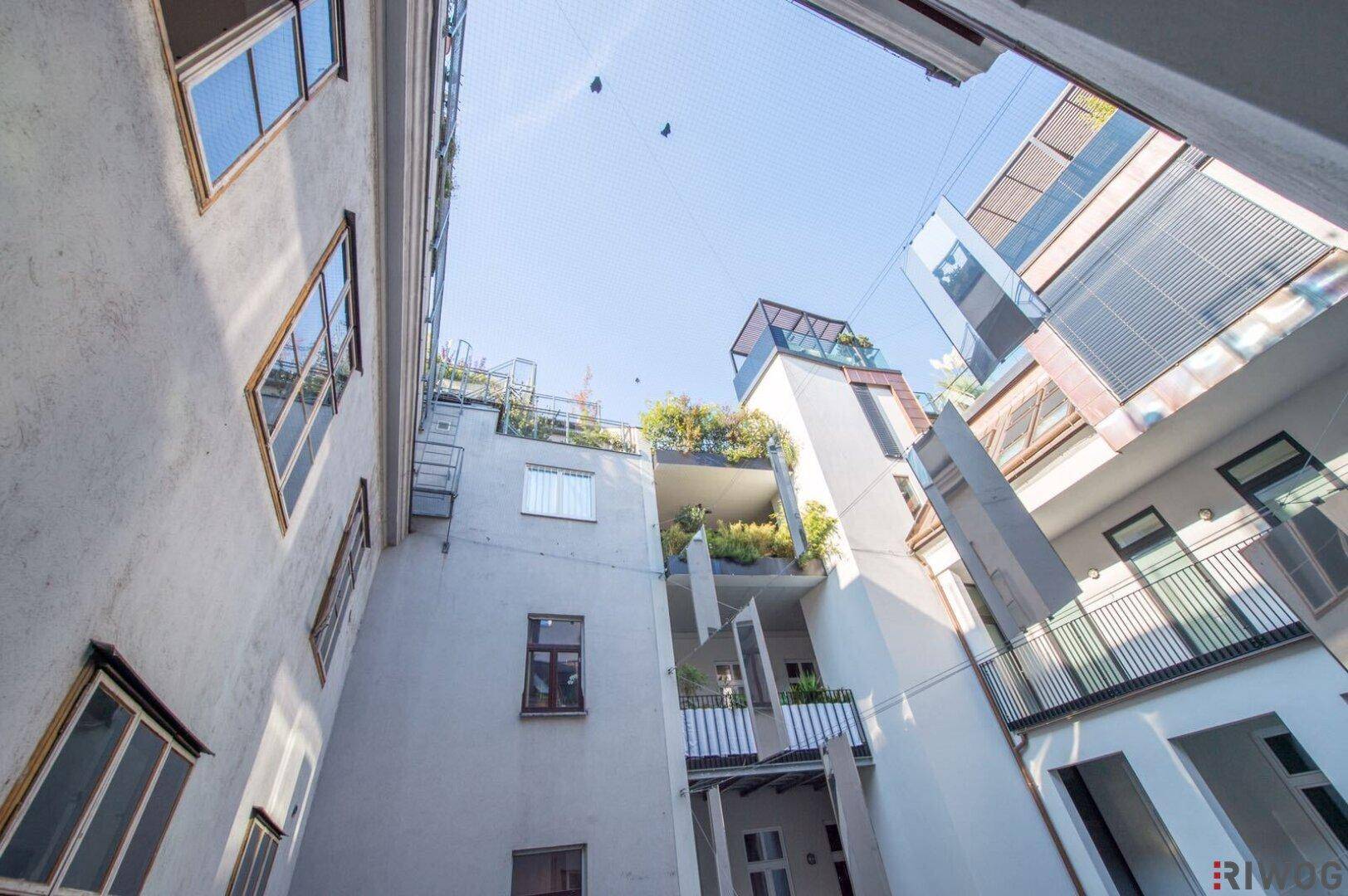 Blick nach oben in einen hellen Innenhof mit modernen Gebäudefassaden und blauen Himmel.