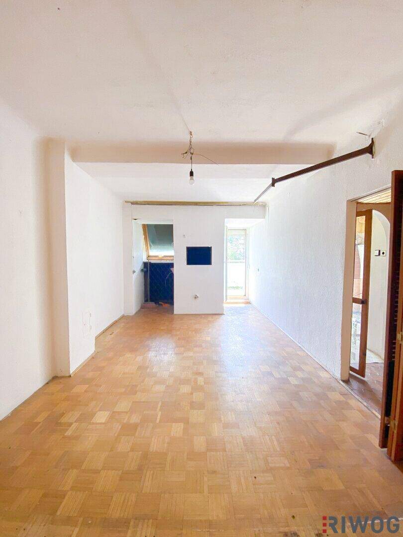 Leerer Raum mit Parkettboden und weißen Wänden, bereit für eine Renovierung und neue Gestaltung.