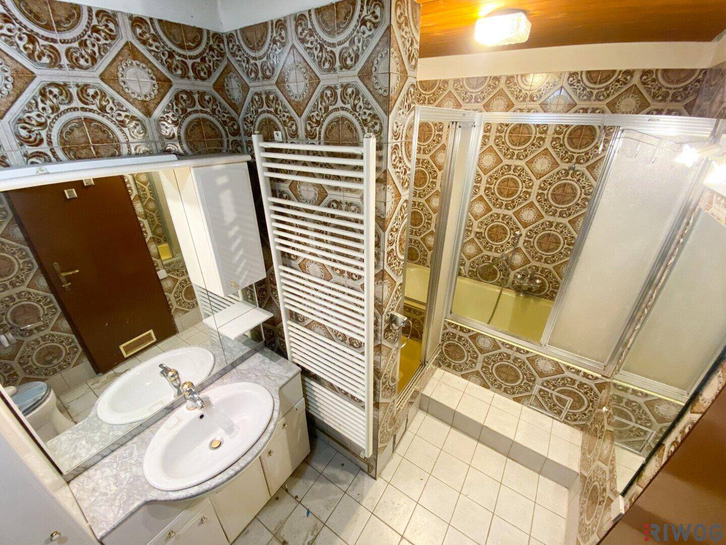 Badezimmer im Stil der 80er Jahre mit gemusterten Fliesen, Doppelwaschbecken und Duschkabine.