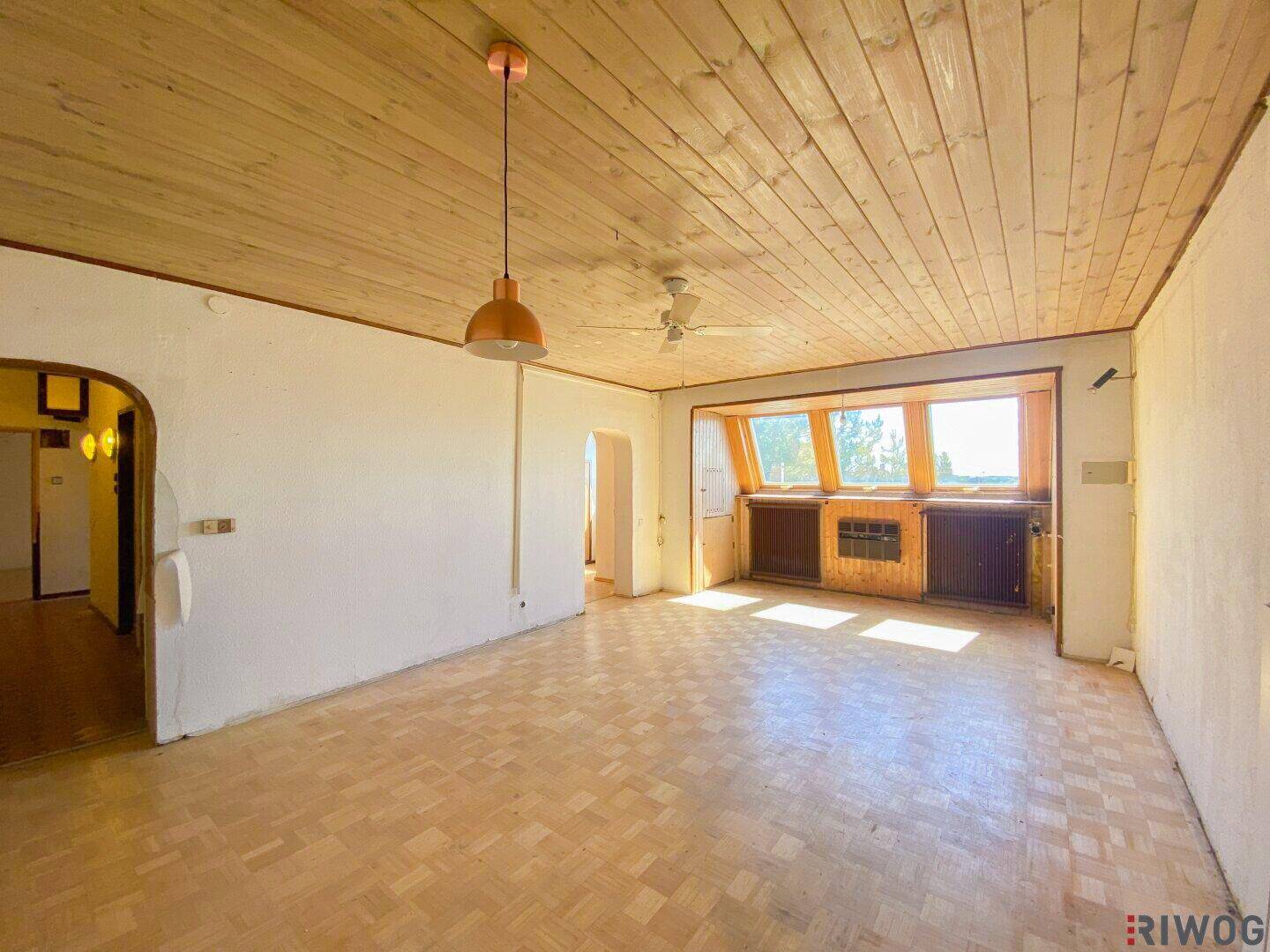 Geräumiges Wohnzimmer mit Holzdecke, Parkettboden, Deckenventilator und großen Fenstern für viel Tageslicht.