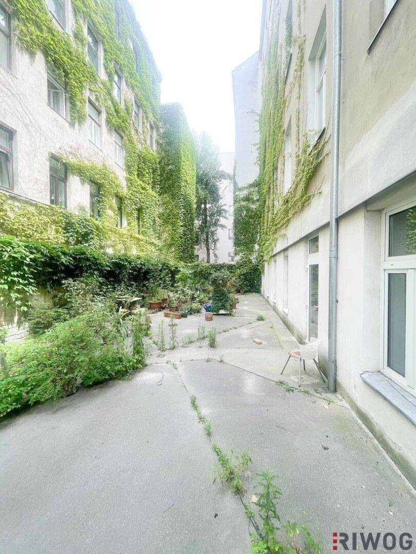 Innenhof mit üppiger Begrünung an den Fassaden und einem gepflasterten Weg.