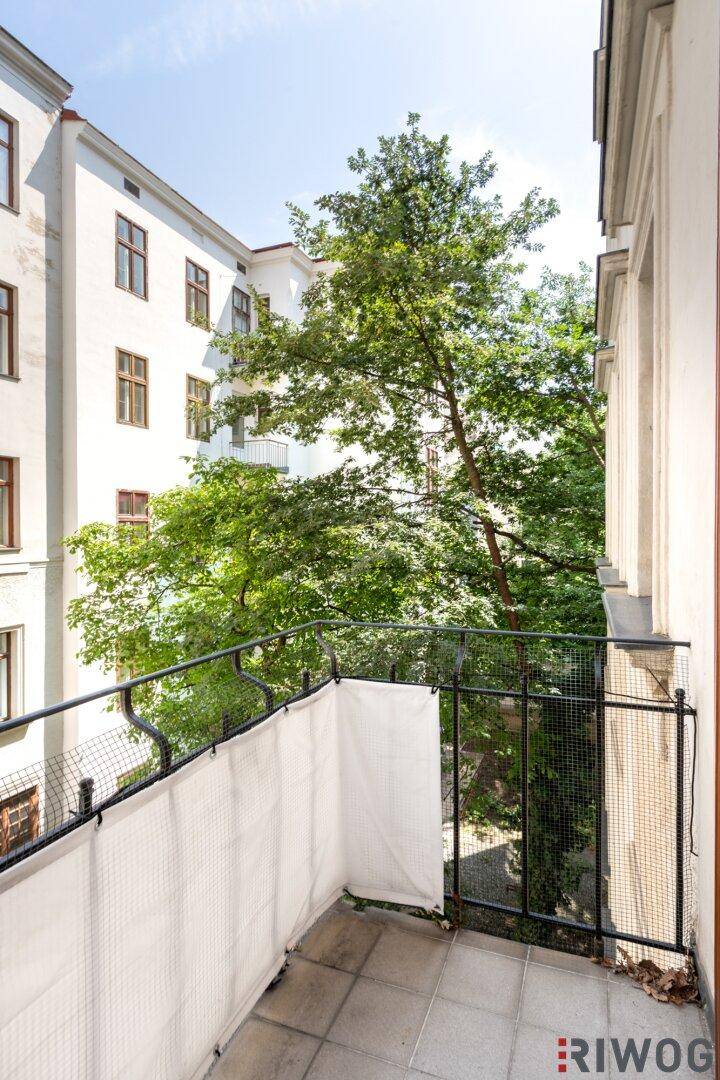 Gemütlicher Balkon mit Gittergeländer und Blick auf den grünen Innenhof des Gebäudes.