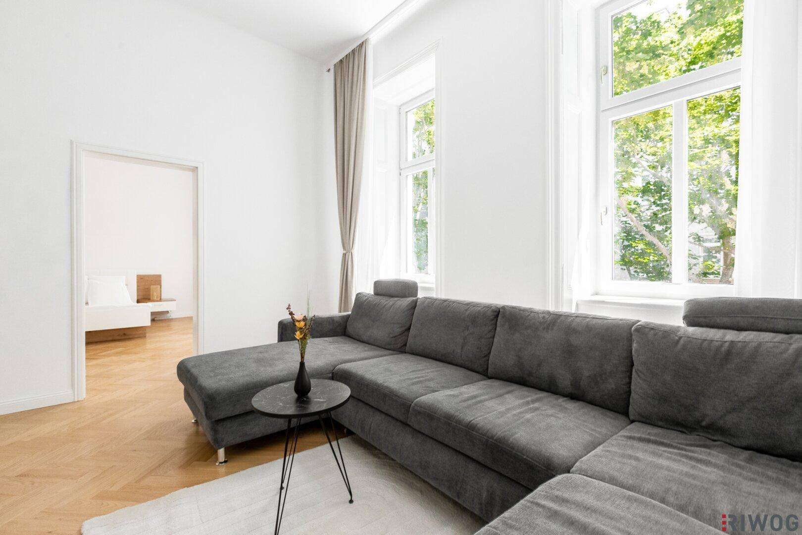 Gemütliches Wohnzimmer mit großem Ecksofa und viel Tageslicht durch hohe Fenster.