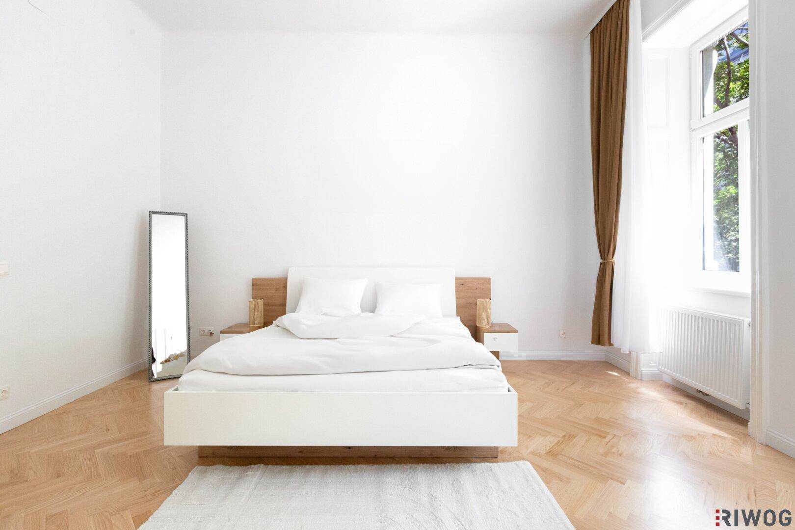 Geräumiges Schlafzimmer mit Doppelbett, Parkettboden und großen Fenstern.