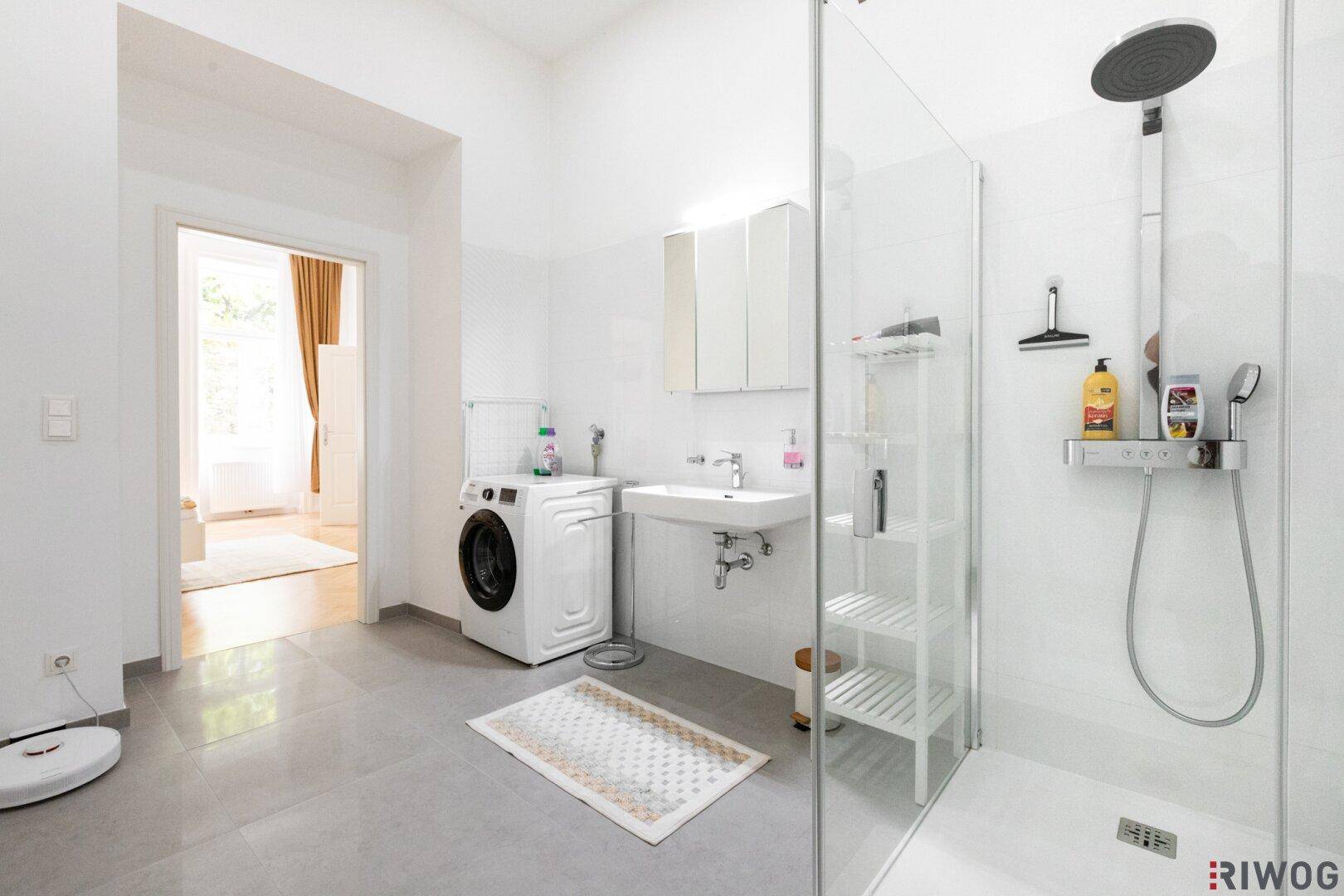 Helles Badezimmer mit großer Dusche, Waschmaschine und Zugang zum Wohnbereich.