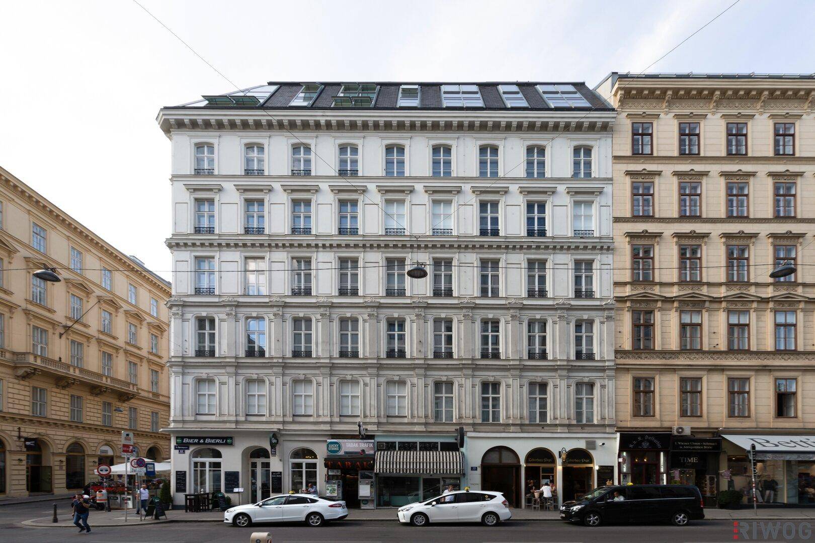 Frontansicht des eleganten Altbaus mit Geschäften im Erdgeschoss und Dachfenstern.