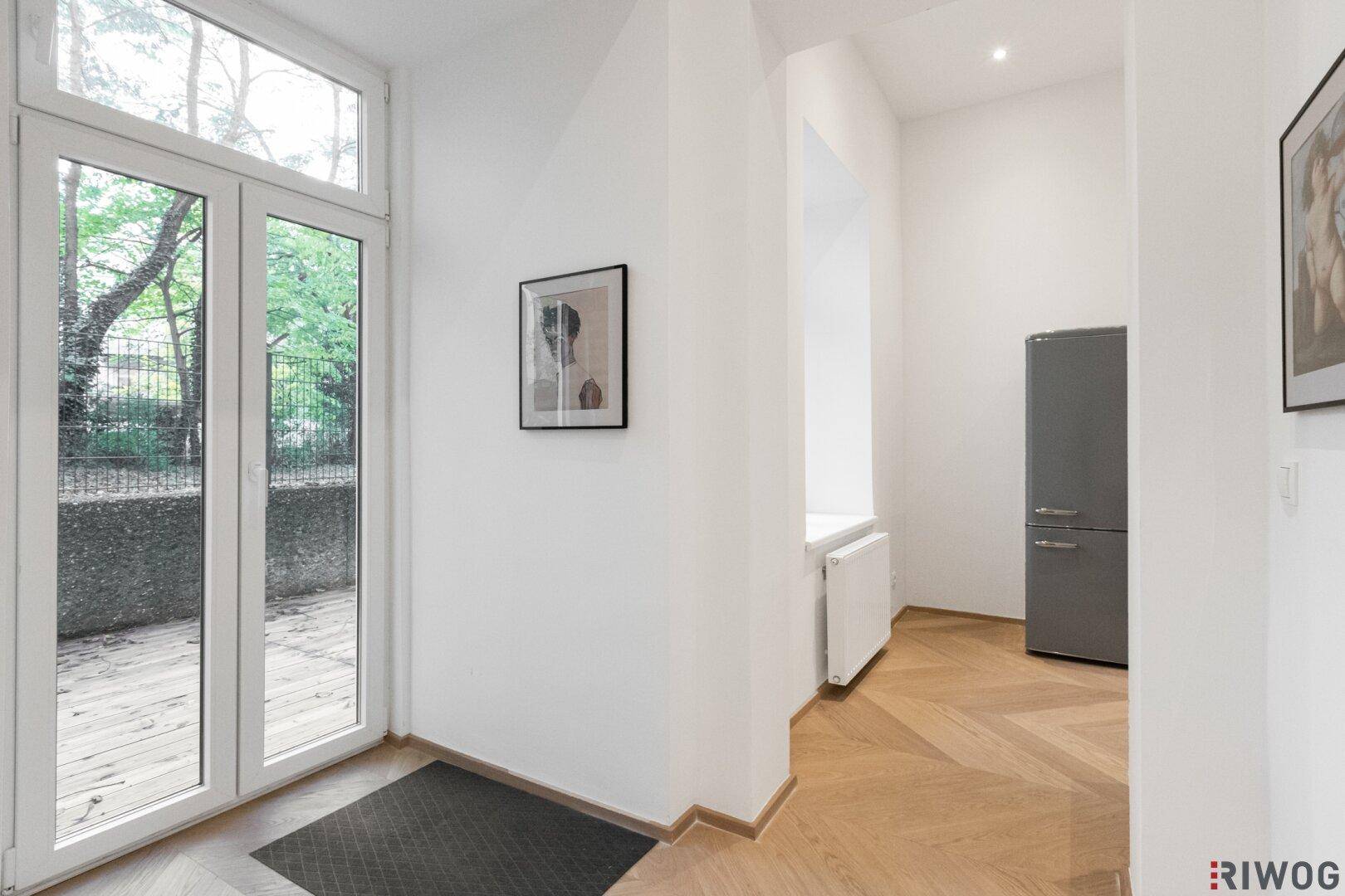 Eingangsbereich mit großen Glastüren, die zu einem Außenbereich führen, und einem freistehenden Kühlschrank.