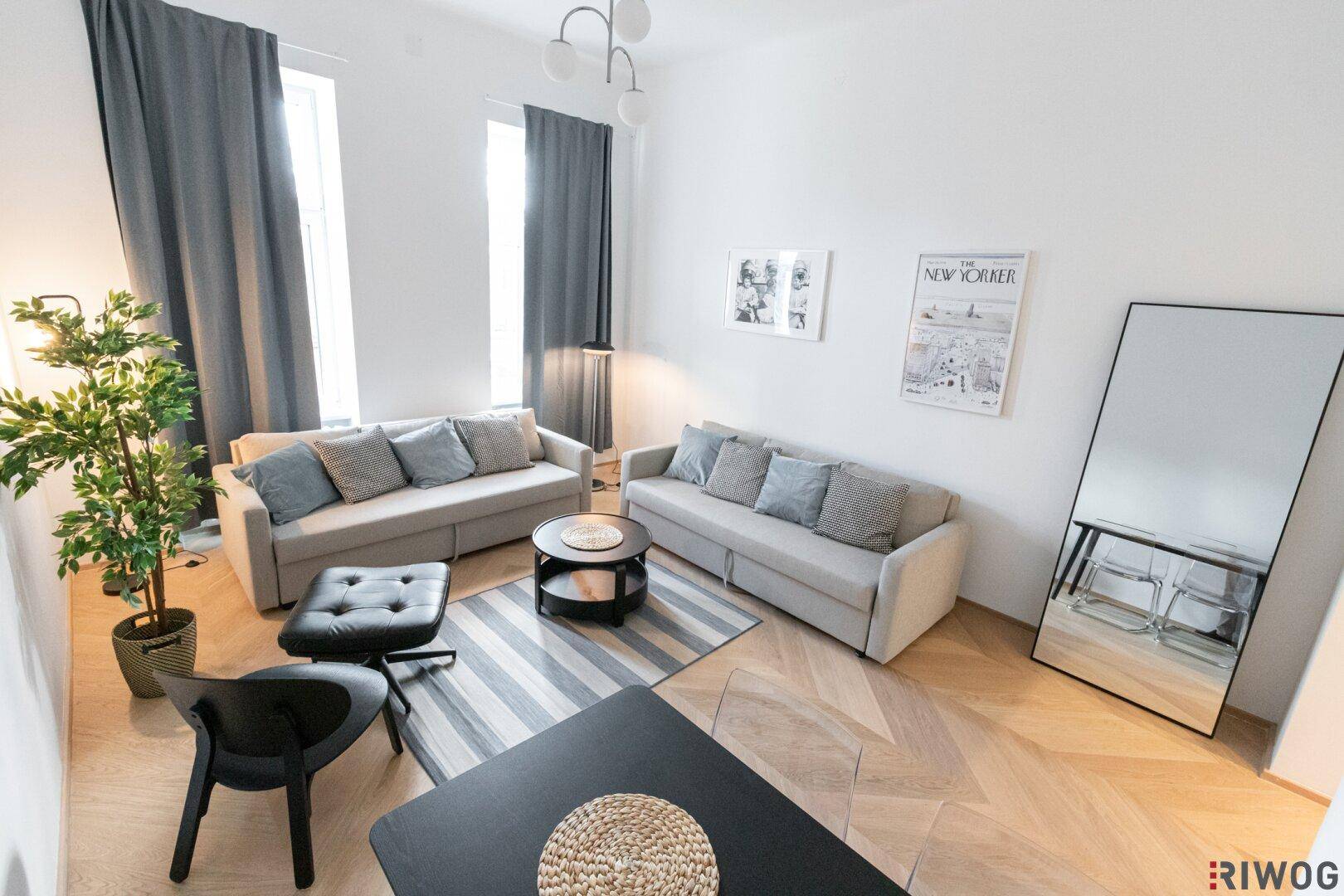 Helles Wohn- und Esszimmer mit zwei Sofas, Holzboden und modernem Teppich.
