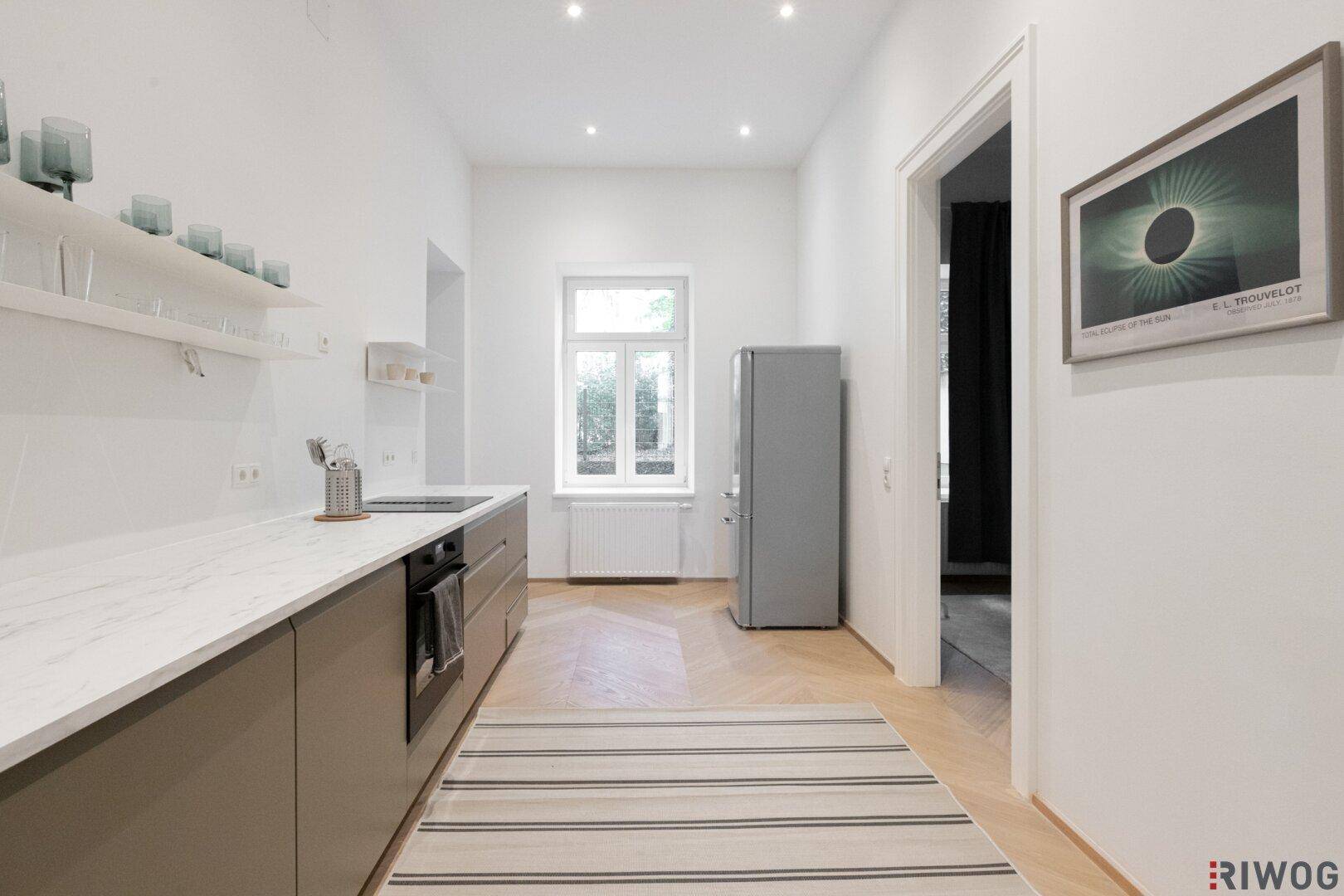 Moderne Küche mit grauen Unterschränken, weißer Arbeitsplatte und Fensterblick.