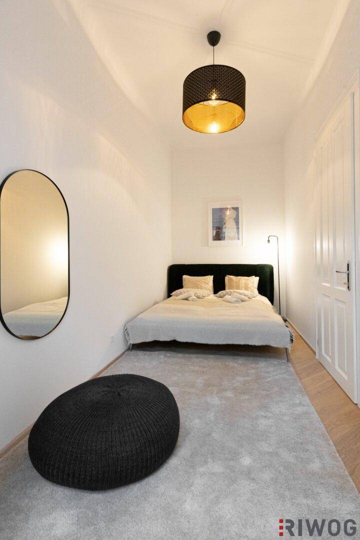 Helles Schlafzimmer mit Bett, großem Teppich und ovalem Spiegel an der Wand.