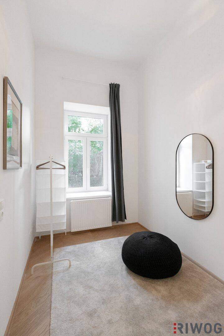 Schlafzimmer mit Fenster, Teppich und Kleiderständer, bietet viel natürliches Licht.