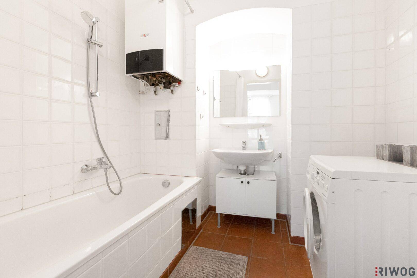 Badezimmer mit Badewanne, Waschbecken, Waschmaschine und weißen Fliesen.